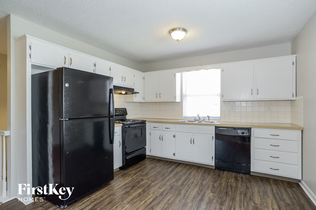 A black refrigerator in a kitchen with wooden floors and white cabinets.