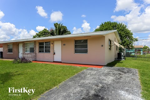 a small pink house with a lawn and a driveway
