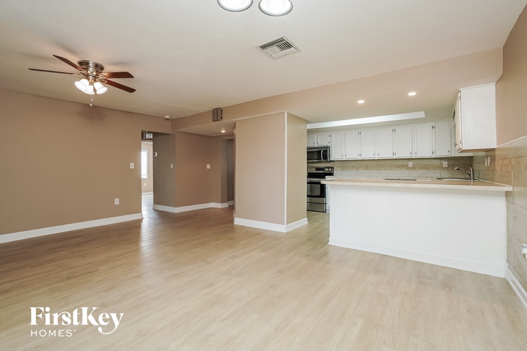 A spacious kitchen and living room with wooden floors and a ceiling fan.