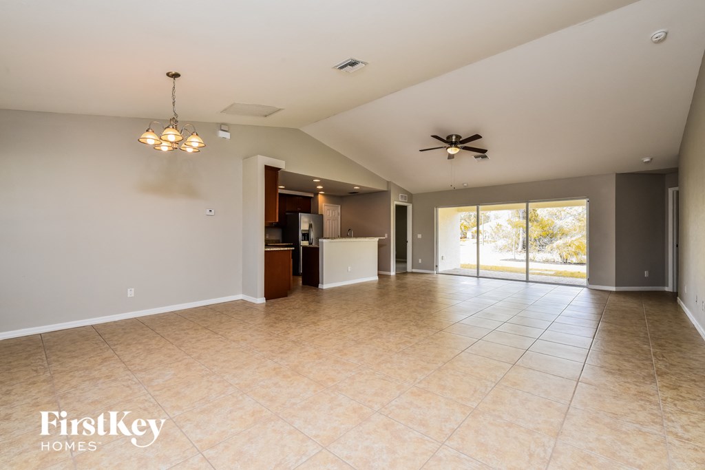 A spacious living room with a kitchen in the background and a ceiling fan.