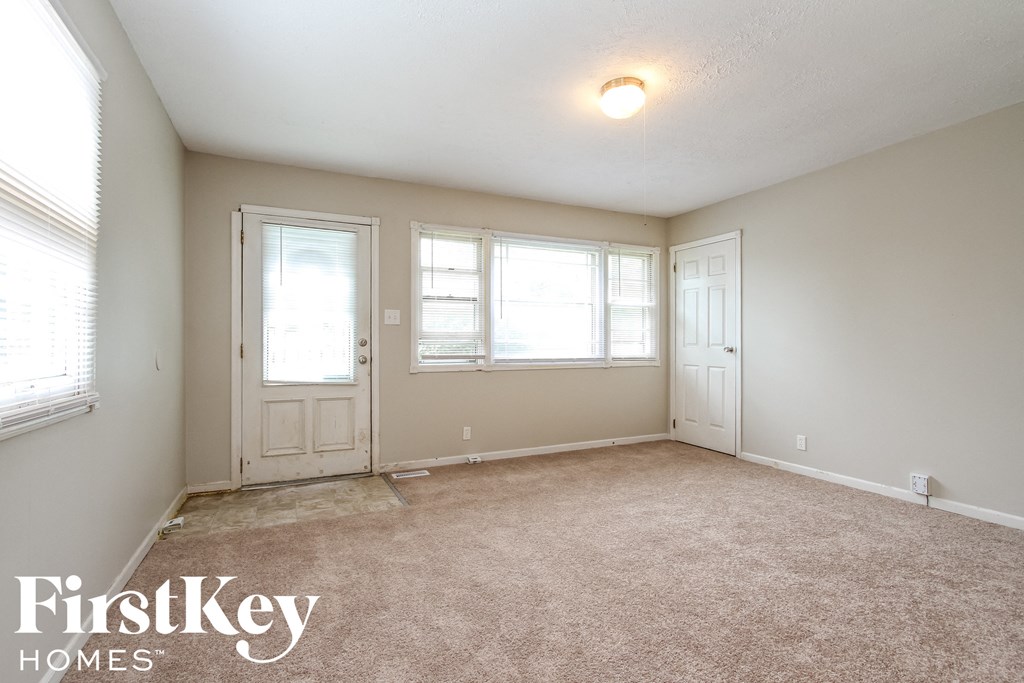 the living room of an empty house with a carpeted floor and three windows