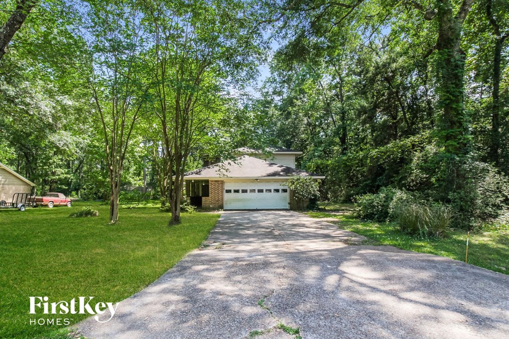 A driveway leads to a garage in a lush green backyard.