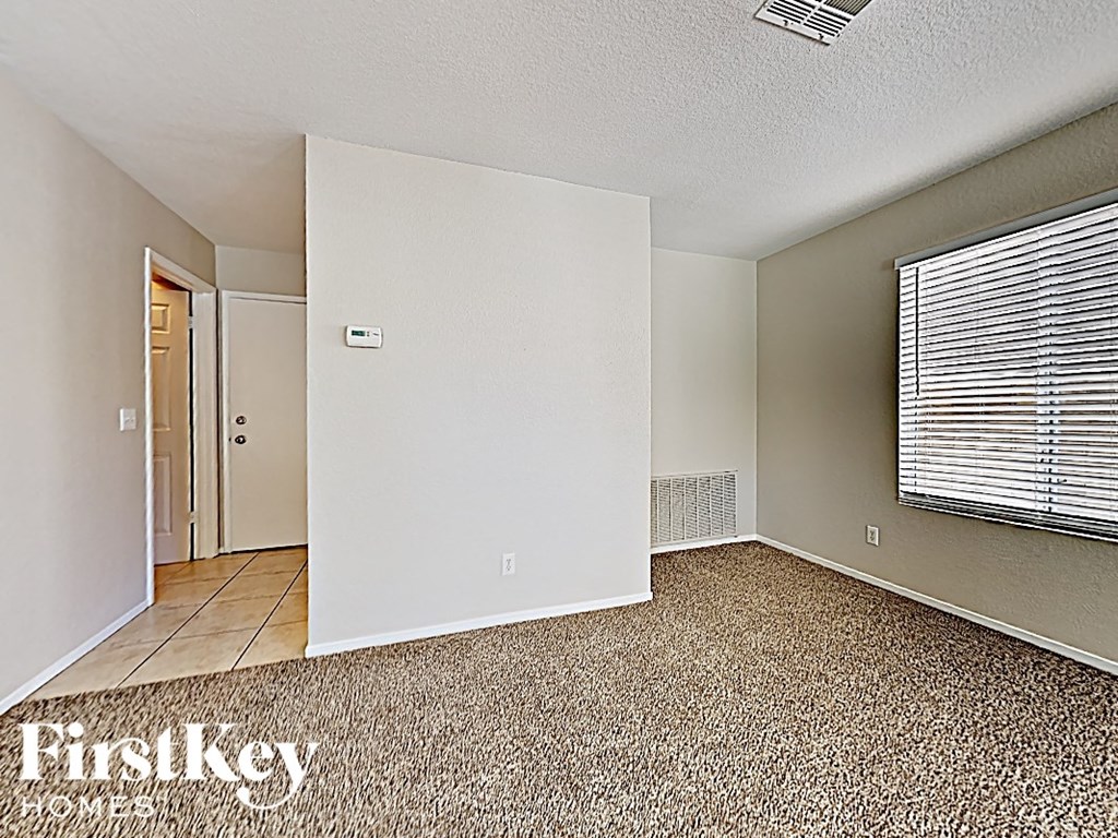 A room with a carpeted floor and a window with blinds.