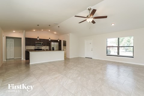 A spacious living room with a kitchen in the background and a ceiling fan above.
