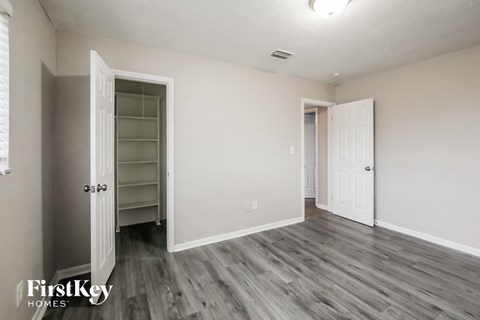 a bedroom with white walls and a closet and wood flooring