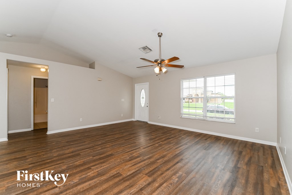the living room of an empty house with wood flooring and a ceiling fan
