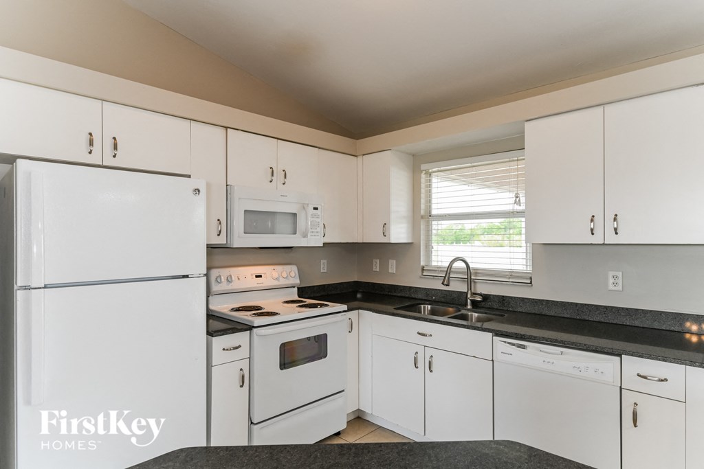 a kitchen with white cabinets and white appliances and black counter tops