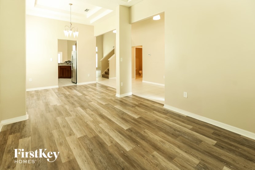 A spacious room with wooden flooring and a staircase in the background.