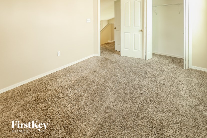 A carpeted room with a door and a staircase in the background.