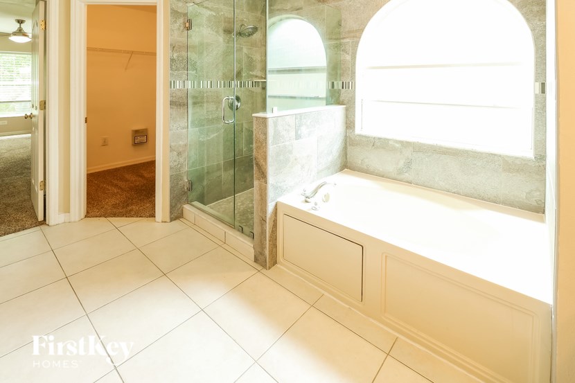 A bathroom with a glass shower enclosure and a bathtub with a window above it.