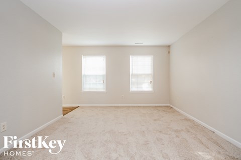 a spacious living room with carpet and two windows