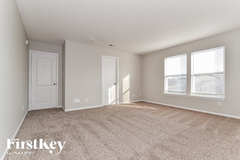 A spacious room with a carpeted floor and two windows.