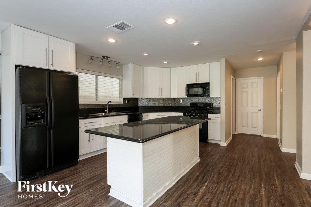 a white kitchen with black counter tops and a black refrigerator