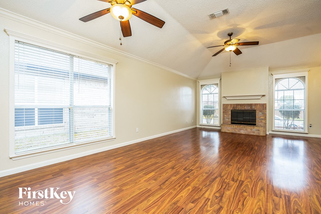 an empty living room with a fireplace and two ceiling fans