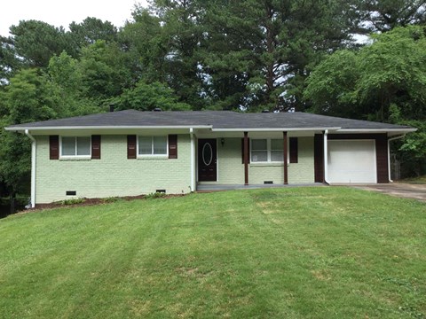 the front of the house with a lawn and trees