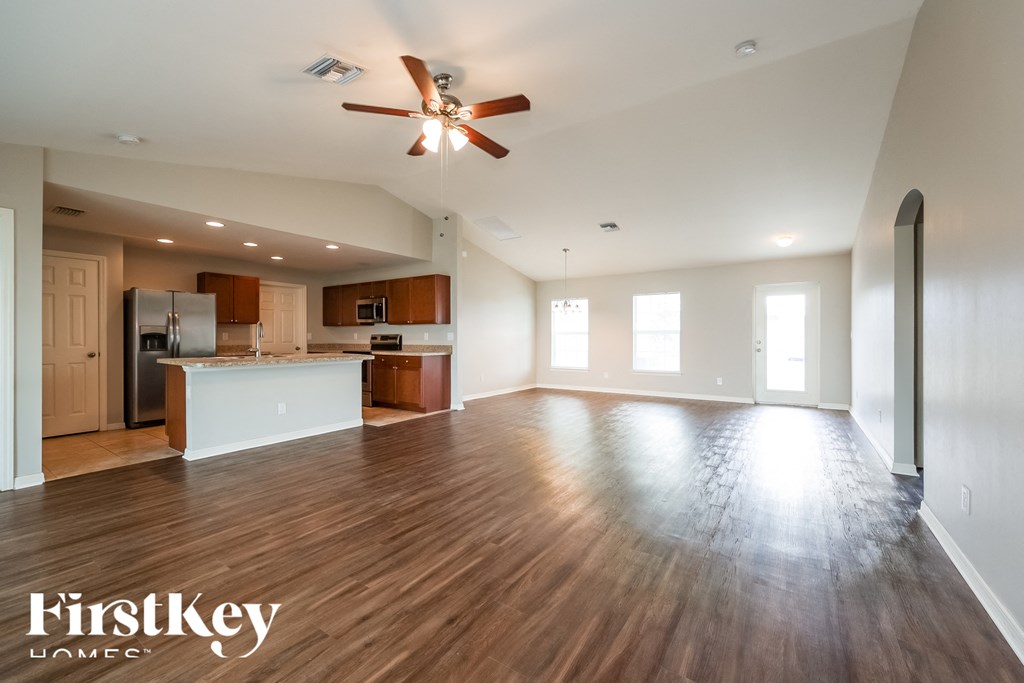 A spacious kitchen and living room with wooden floors and a ceiling fan.
