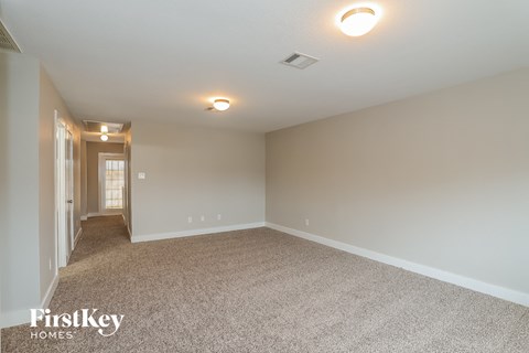 a spacious living room with carpet and a door to a hallway