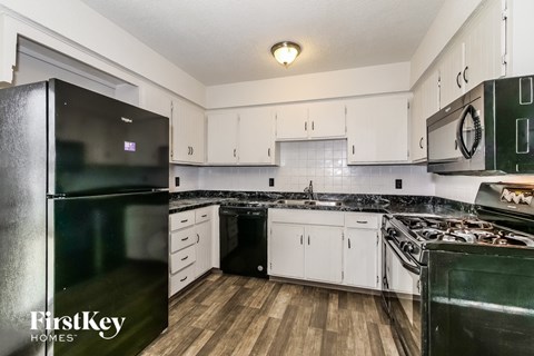 A kitchen with a black fridge and stove top oven.