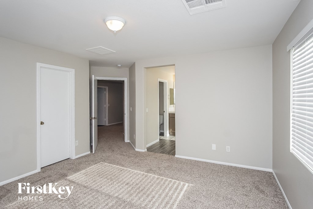 a bedroom with a carpeted floor and a hallway with a door to a bathroom