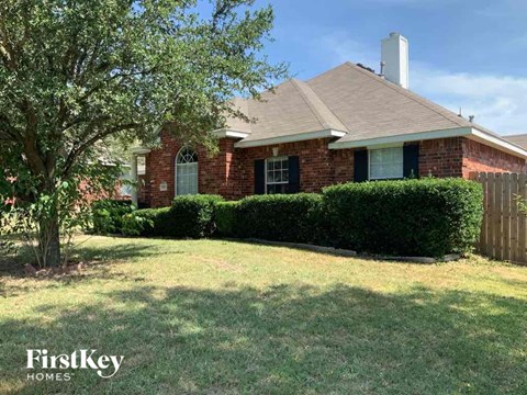 the front of a brick house with a yard and a tree