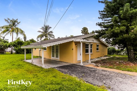 a small yellow house with a driveway and a palm tree