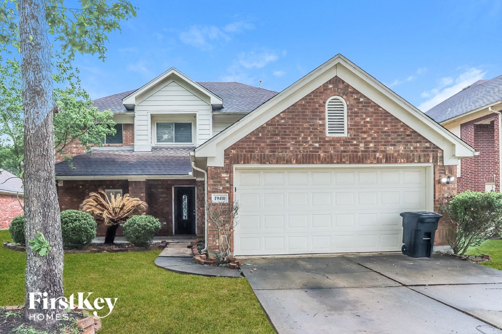 A brick house with a white garage door and a black trash bin in front.