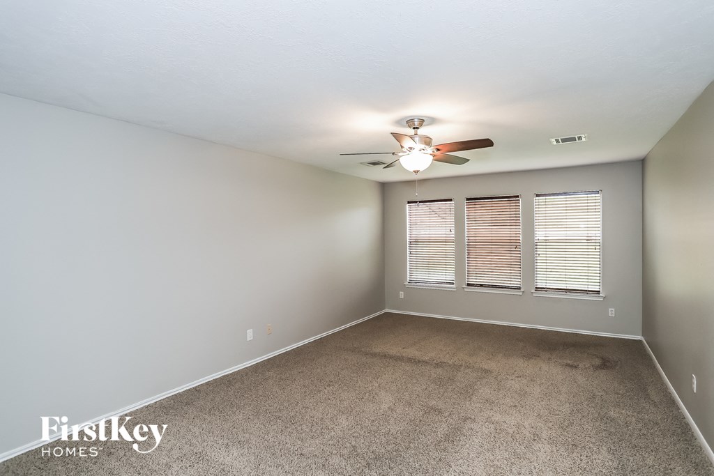 A room with a carpet floor, a ceiling fan, and a window with blinds.
