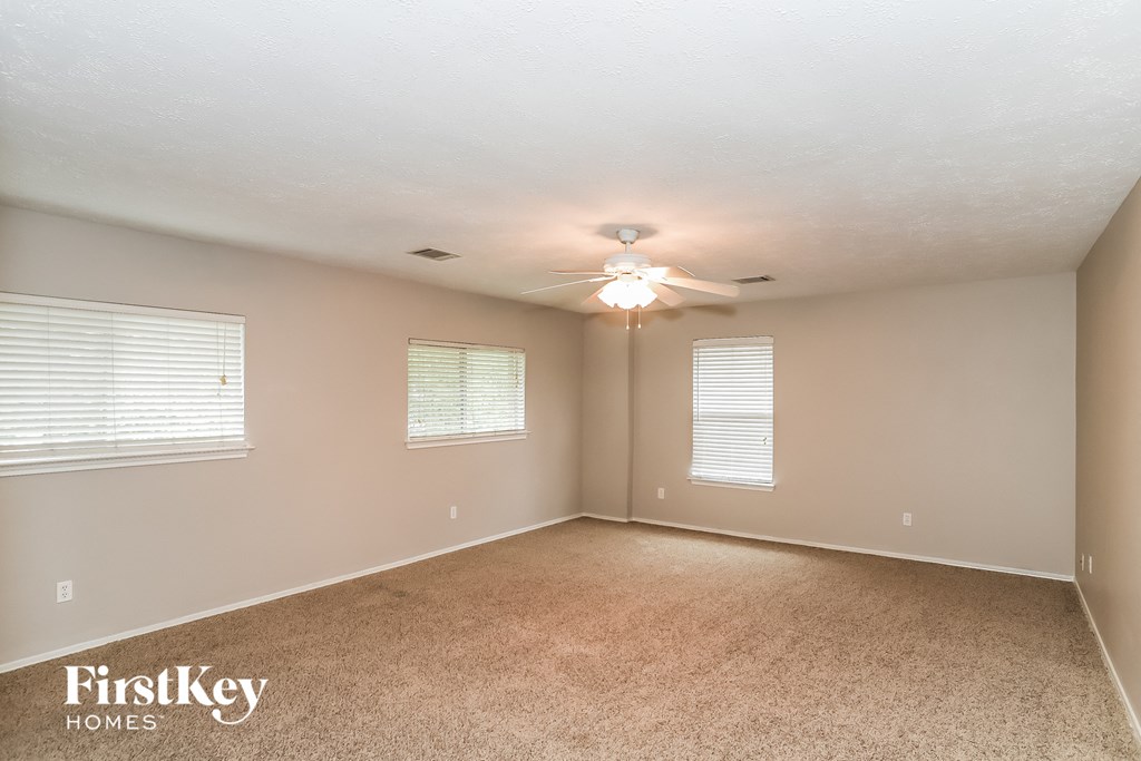 A room with a carpet floor, a ceiling fan, and two windows.