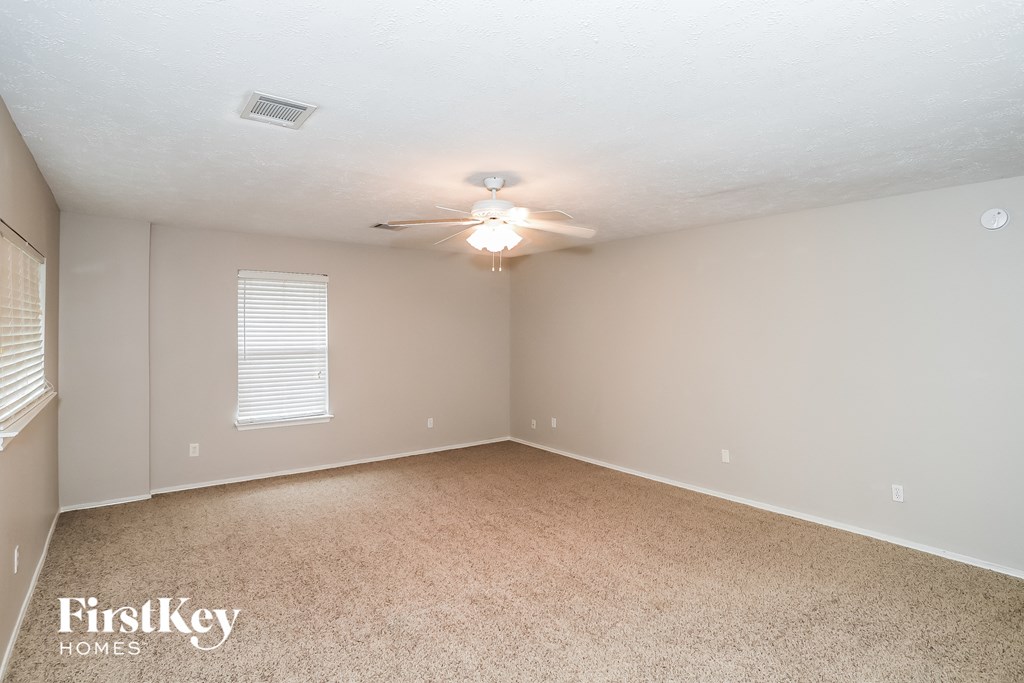 A spacious room with a carpeted floor and a ceiling fan.