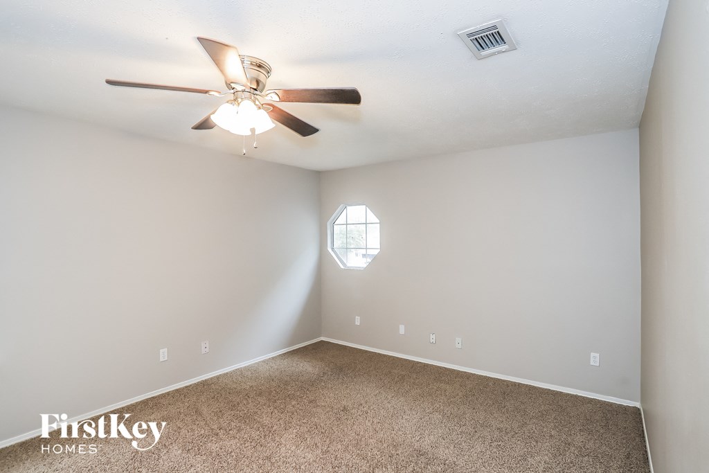 A carpeted room with a ceiling fan and a window.