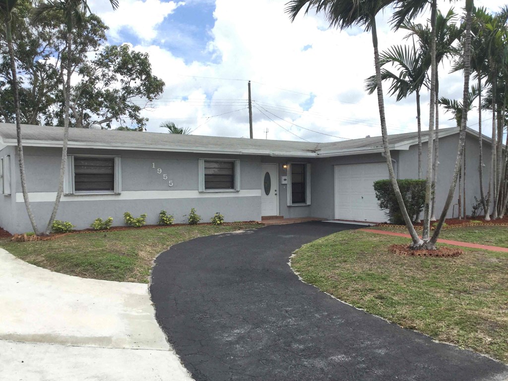 the front of a white house with a driveway and palm trees