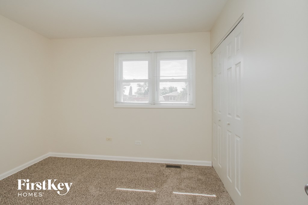 A room with a carpeted floor and a window with blinds.