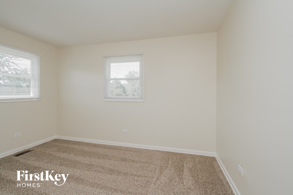 A room with a carpeted floor and two windows.
