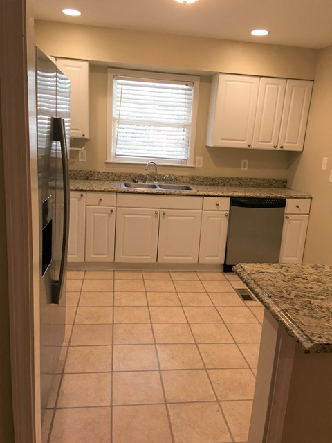 A kitchen with a granite counter top and white cabinets.