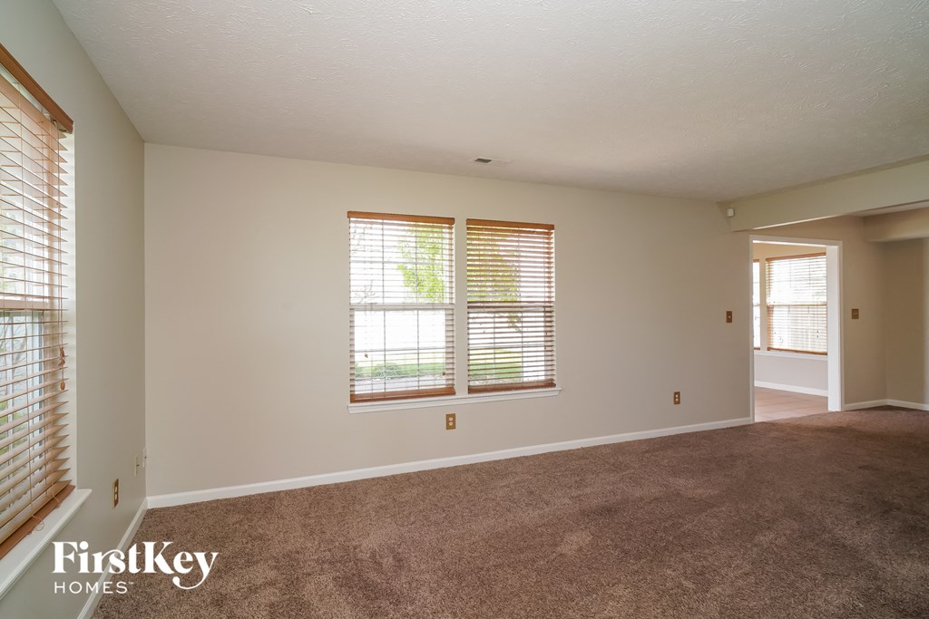 the living room of an empty house with a carpeted floor and two windows