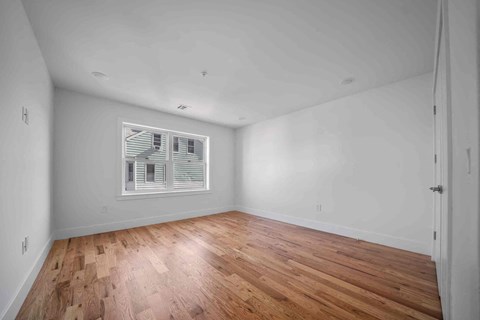 the living room is spacious and has a large window and hardwood floors