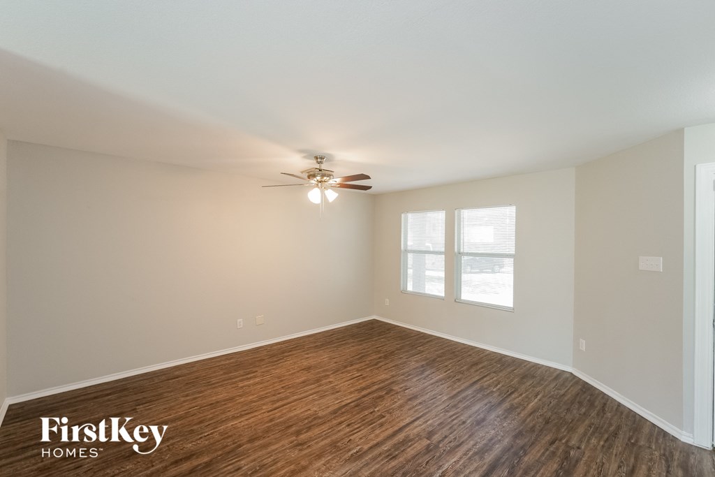 the spacious living room with hardwood flooring and a ceiling fan