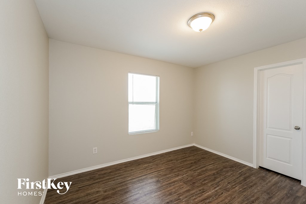 a bedroom with white walls and wood flooring and a window