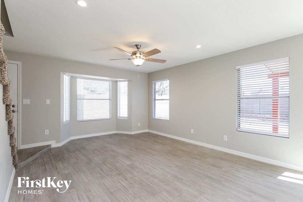 an empty living room with a ceiling fan and windows