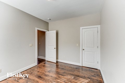 a bedroom with white walls and wooden floors and two doors