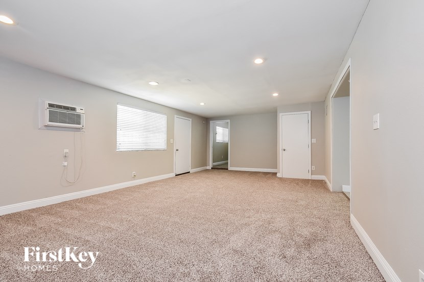 A spacious room with a carpeted floor and a window with blinds.
