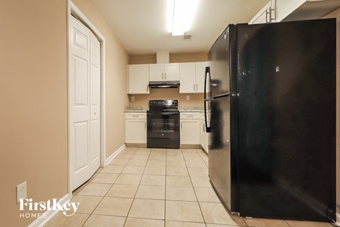 A black refrigerator stands in a kitchen with white cabinets and appliances.