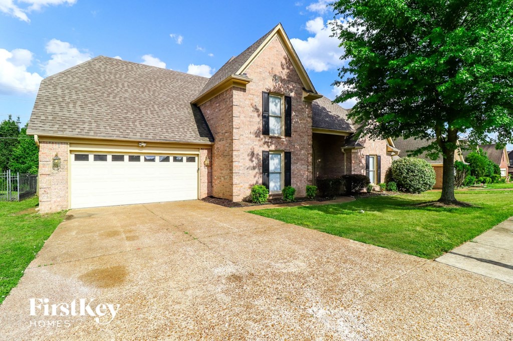 A brick house with a garage and a tree in front.