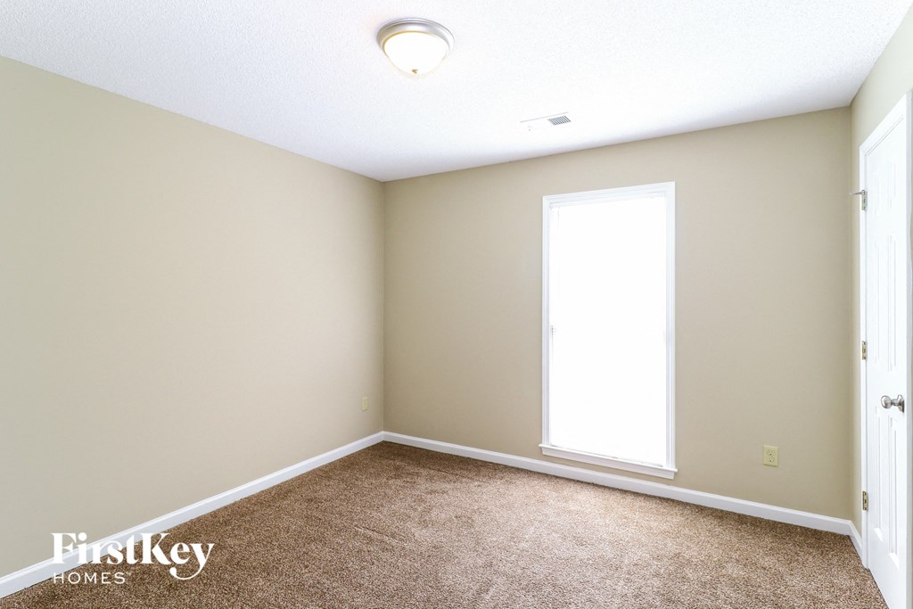 A room with a carpeted floor, a window, and a door.