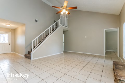 A spacious room with a staircase and a ceiling fan.