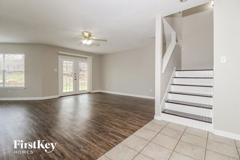 A spacious room with wooden floors and a staircase leading to another room.