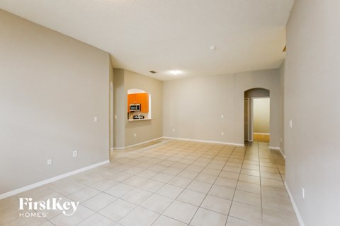 a spacious living room with tiled floors and a hallway to the kitchen