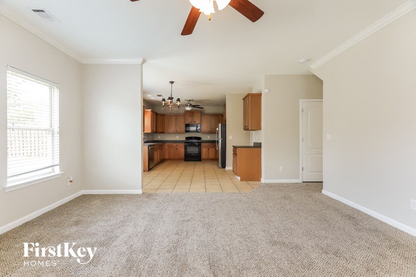 an empty living room with a kitchen in the background