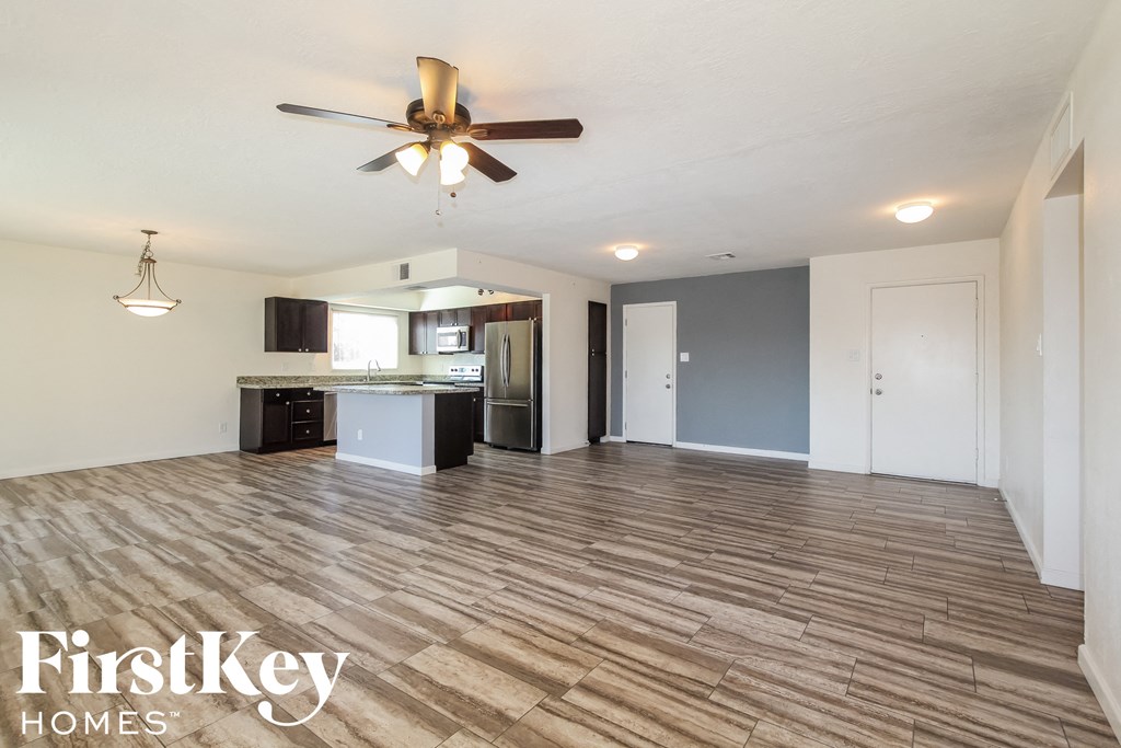 an empty living room with a ceiling fan and a kitchen