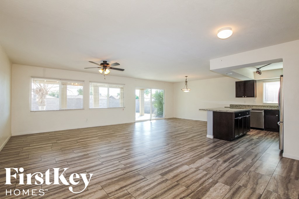 an empty living room with a ceiling fan and a kitchen